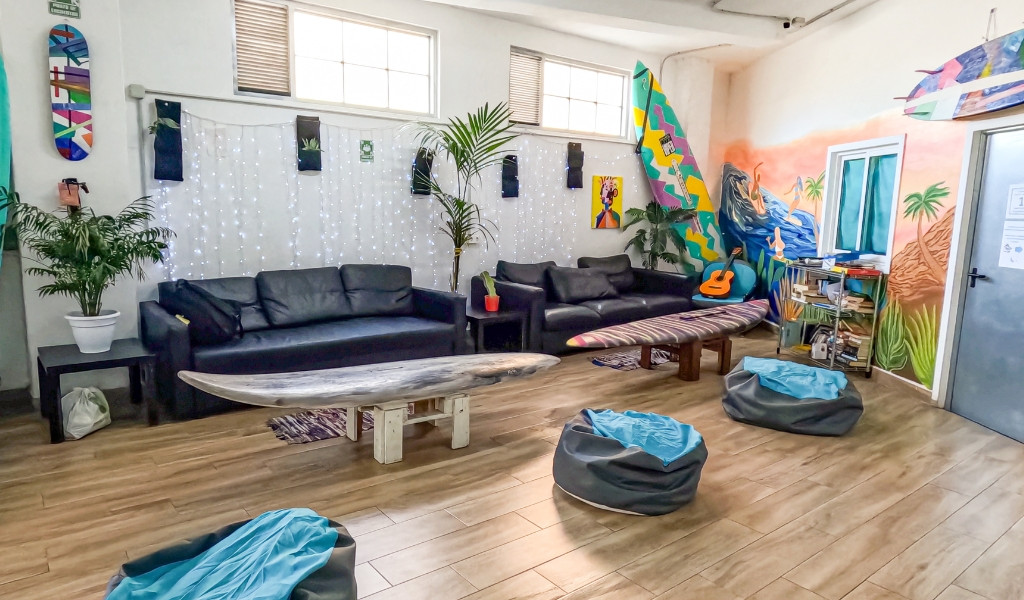 Sala de estar con sofás, tablas de surf y murales coloridos en un hostel en Tenerife.