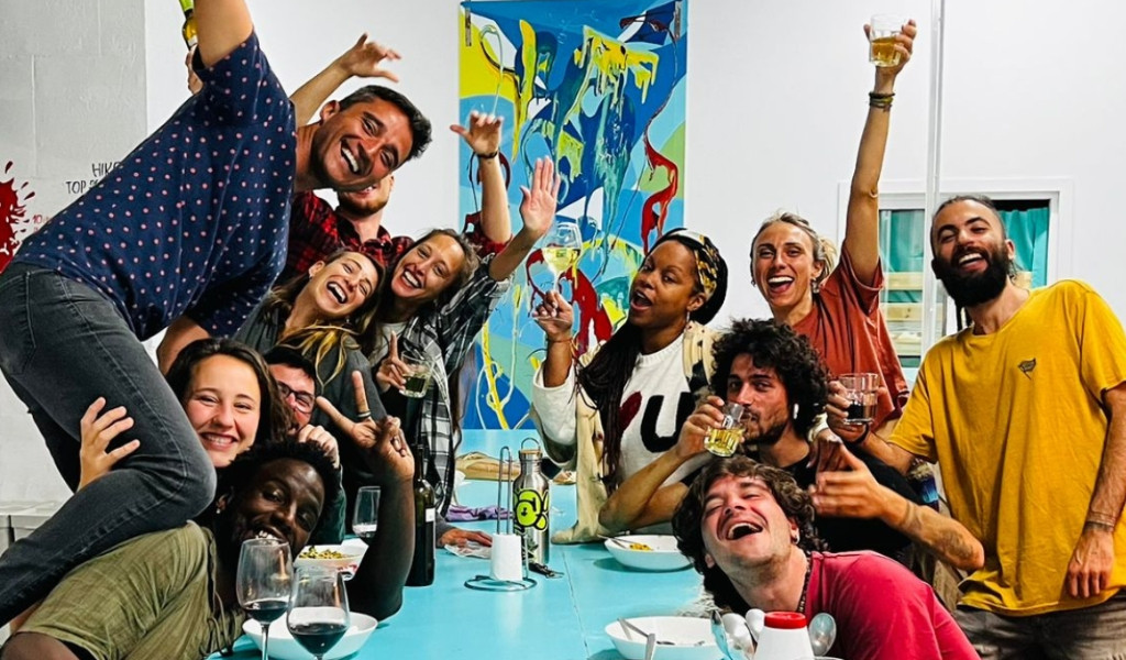 Grupo de amigos celebrando en una mesa con bebidas y un cuadro colorido detrás.