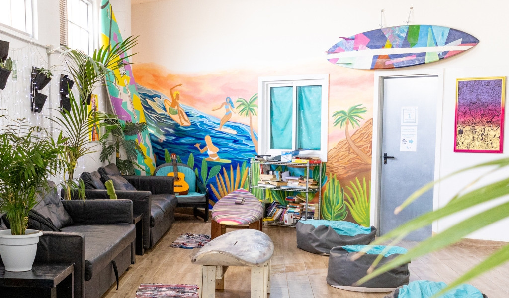 Sala decorada con murales coloridos y plantas en una casa de surf en Tenerife.