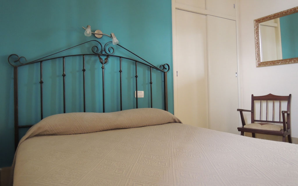 Cama en habitación con cabecera de metal y pared azul en Tenerife.