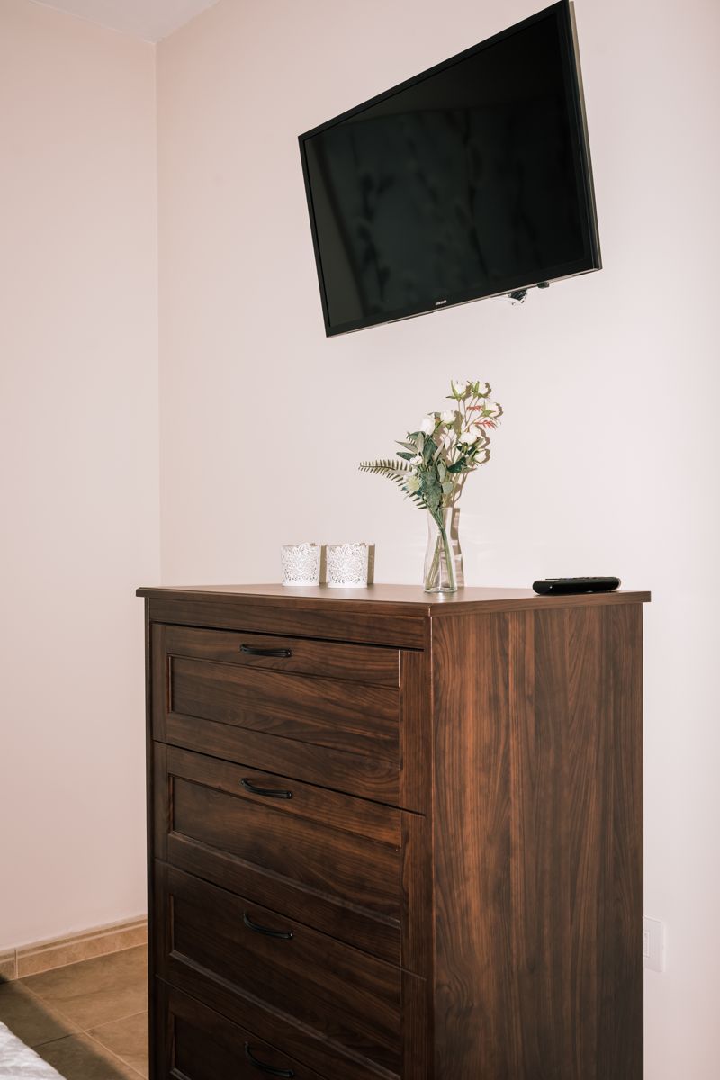 Televisor en pared sobre cómoda con jarrón de flores en una habitación de Tenerife.