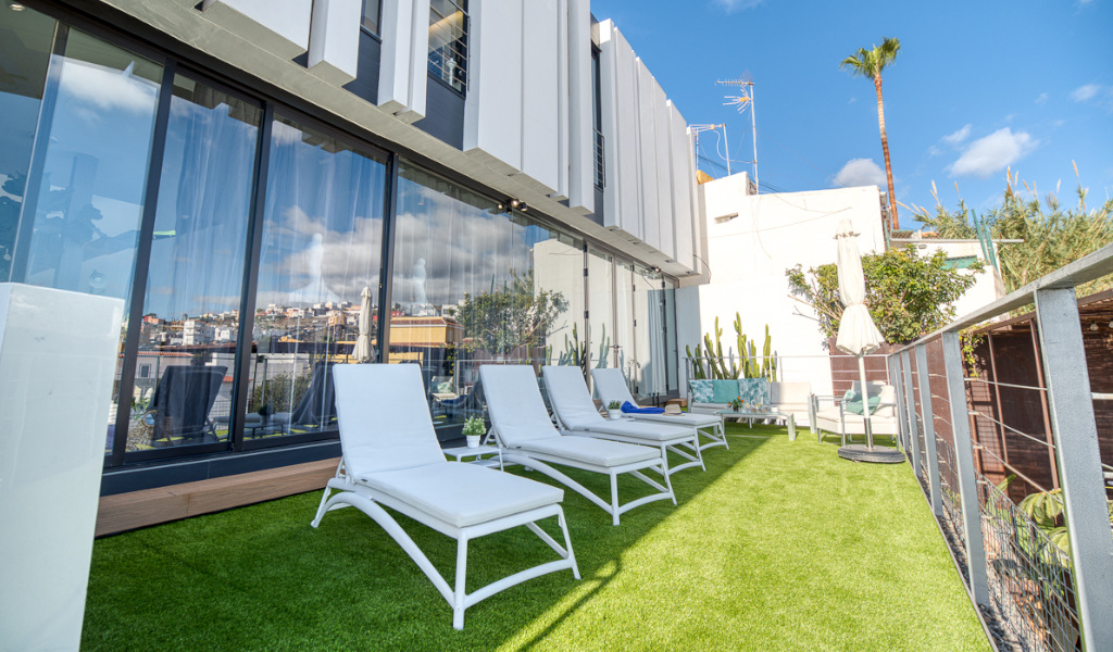 Tumbonas blancas en terraza de Tenerife con paisaje urbano al fondo.