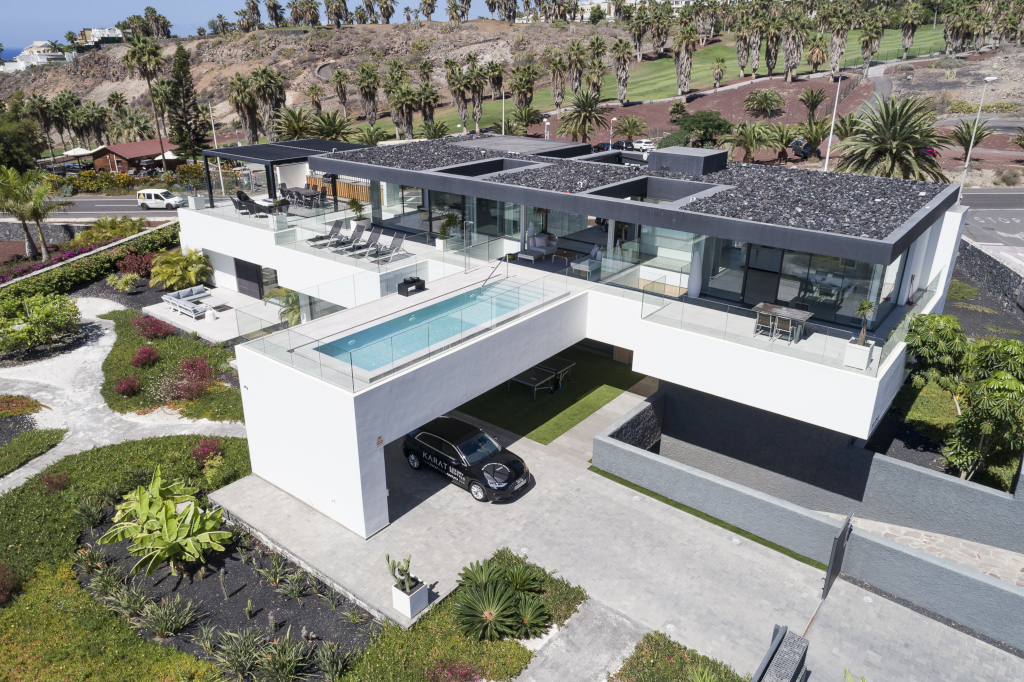 Casa moderna con piscina y coche en entrada, línea de palmeras al fondo en Tenerife.