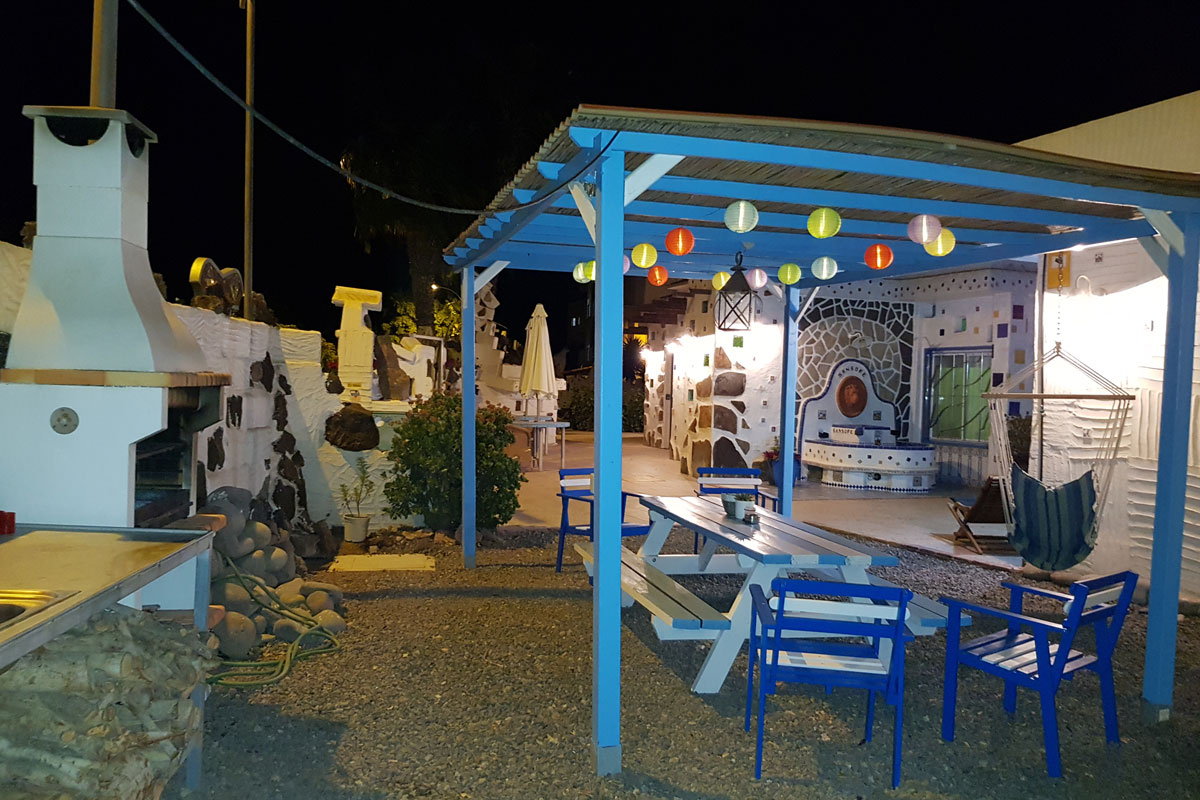 Patio nocturno con barbacoa en Tenerife, decoración colorida y sillas azules.