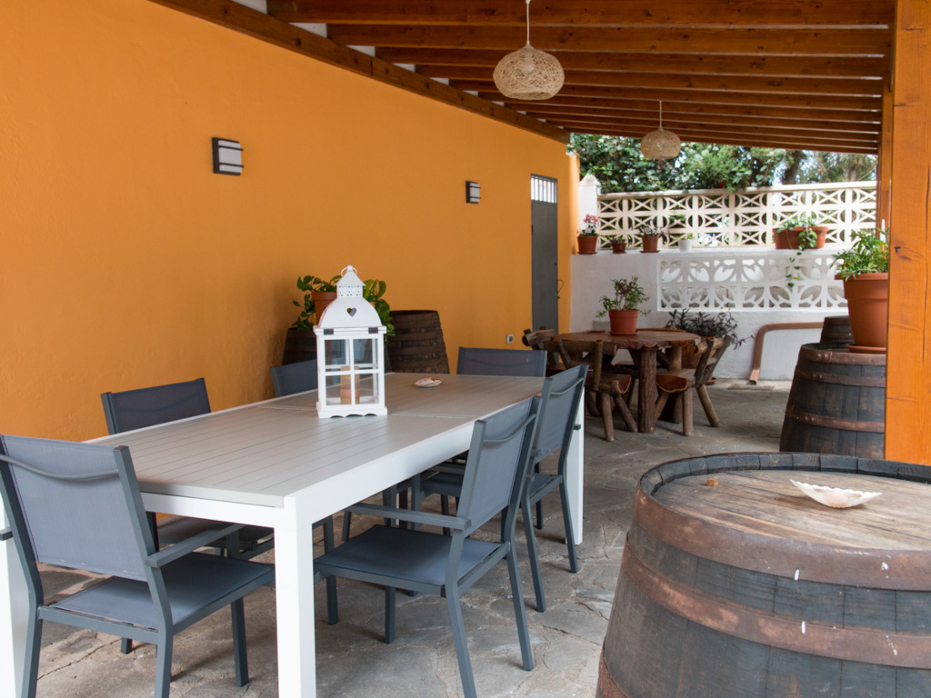 Terraza con mesa y sillas en Tenerife, decorada con plantas y barriles.