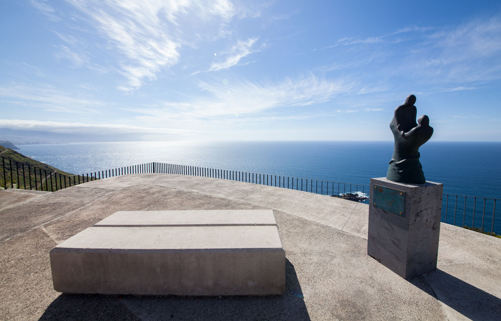 Mirador en Tenerife con escultura y vista al océano Atlántico bajo cielo despejado.