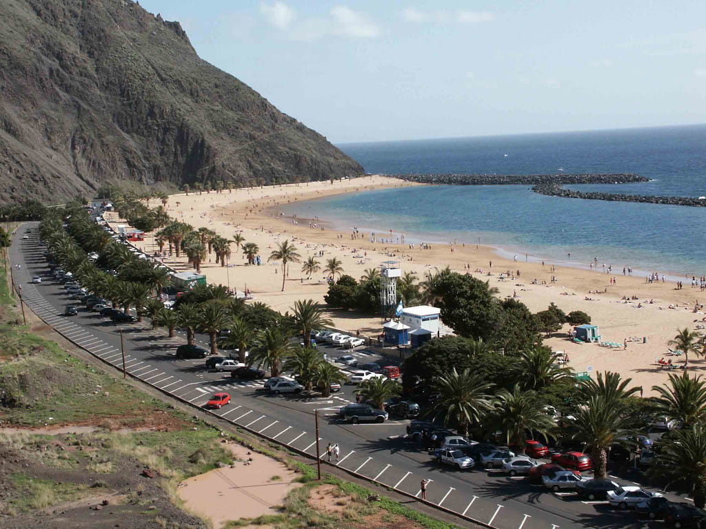 Playa de Las Teresitas en Tenerife con arena dorada y palmeras junto al mar.