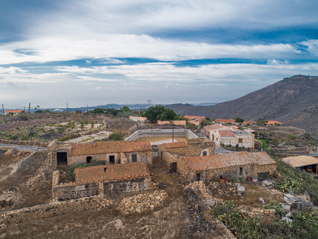 Ruinas de antiguas casas de roca con tejados de teja en Tenerife, rodeadas de campo.