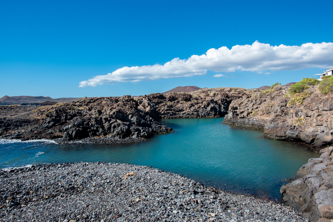 Piscina natural de agua turquesa en Los Abrigos, rodeada de rocas volcánicas.