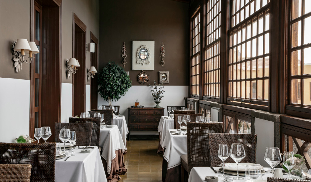 Comedor con mesas y sillas de mimbre frente a ventanas en restaurante de Tenerife.