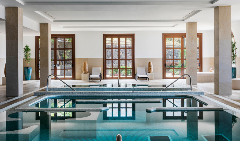 Piscina interior con tumbonas y ventanales en un spa de Tenerife.
