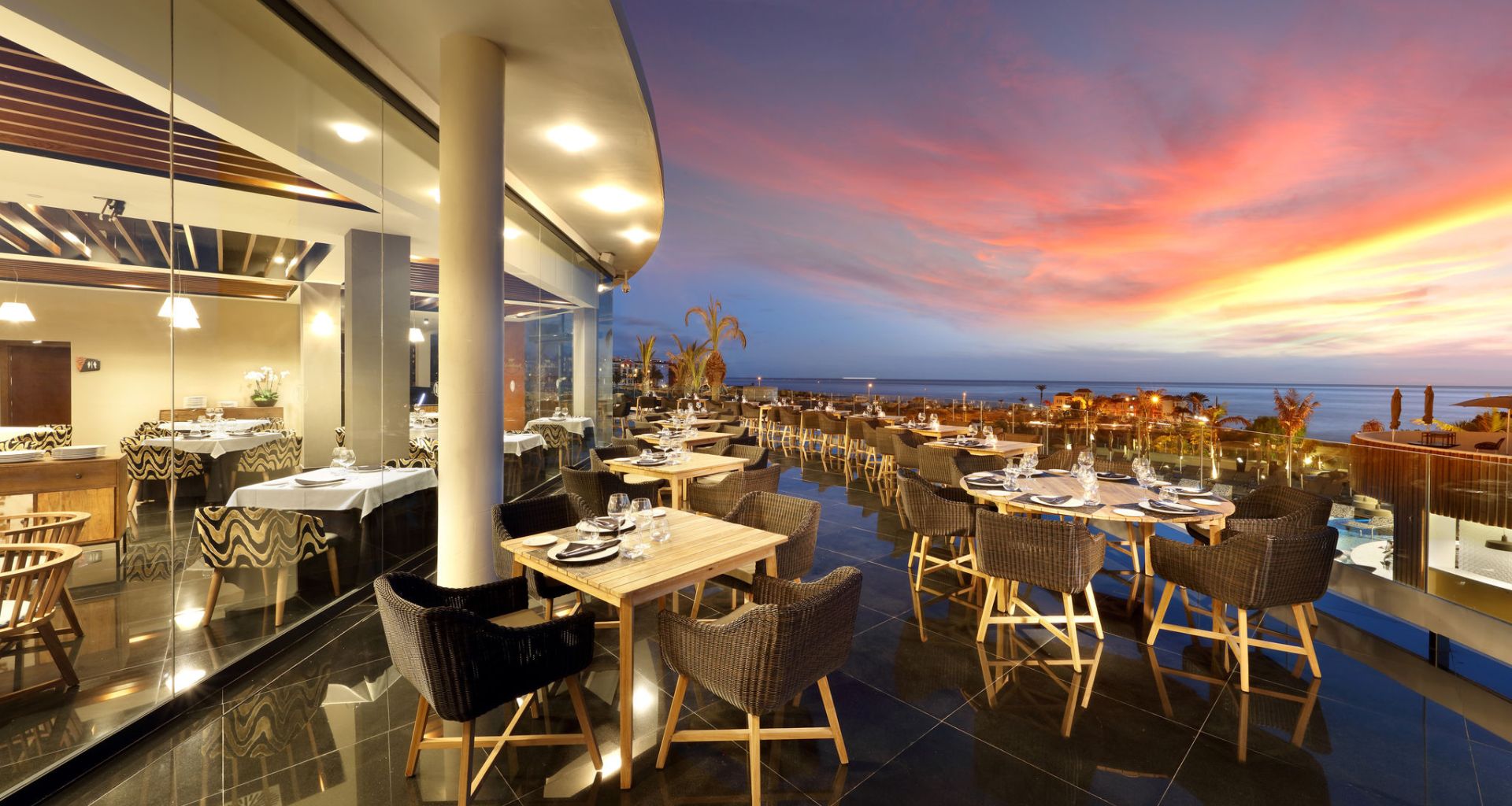 Restaurante con terraza al atardecer en Tenerife, con vista al mar y mesas preparadas.