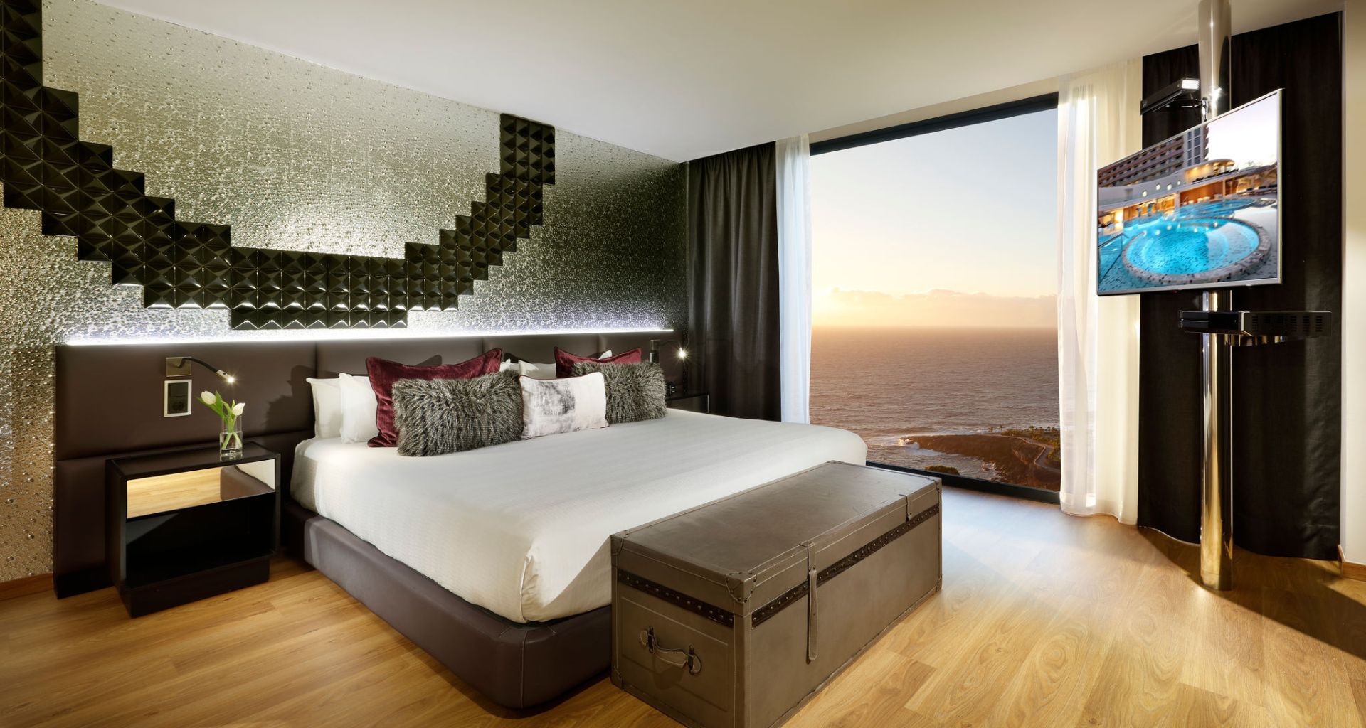 Habitación moderna con cama, televisión y vista al mar al atardecer en Tenerife.