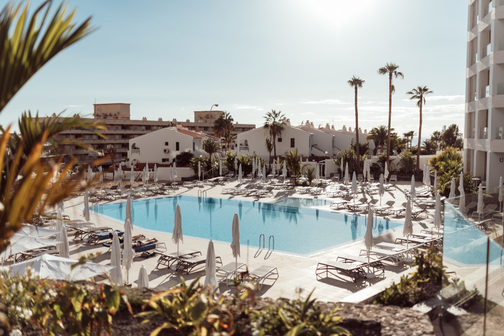 Piscina rodeada de tumbonas y palmeras en hotel de Tenerife.