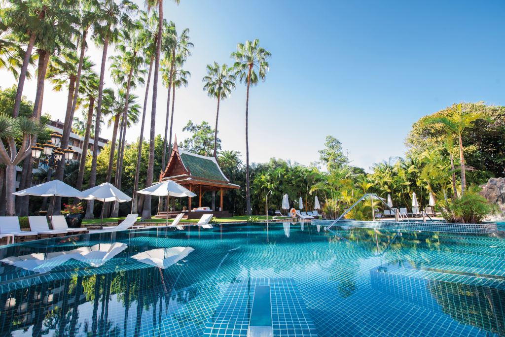 Piscina rodeada de palmeras y cabaña en hotel de Tenerife.