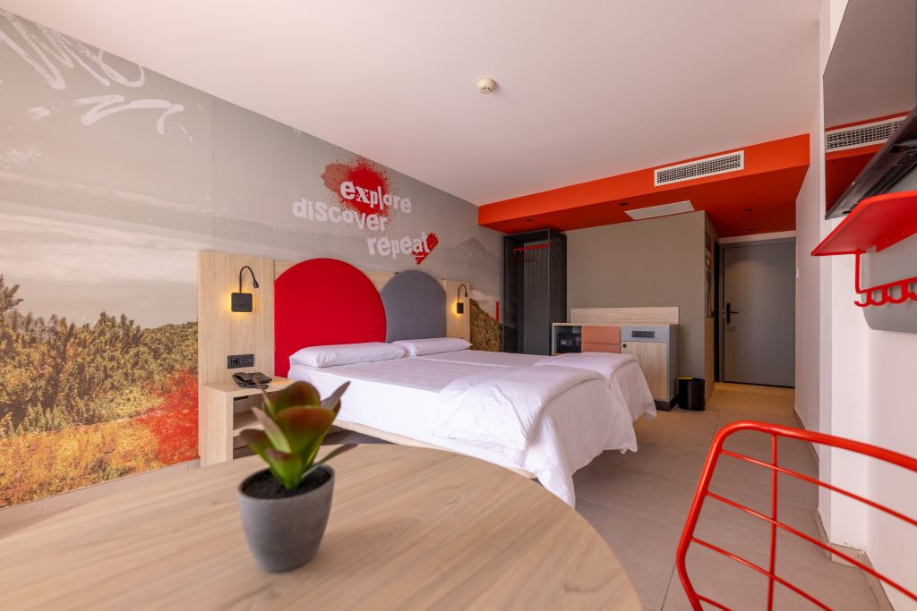 Habitación moderna con cama doble, planta y mural que dice explore discover repeat.