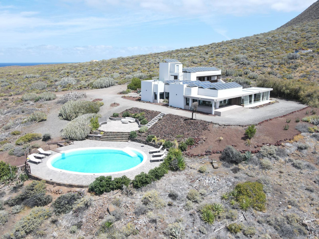 Casa blanca con piscina y paneles solares en el paisaje árido de Tenerife.