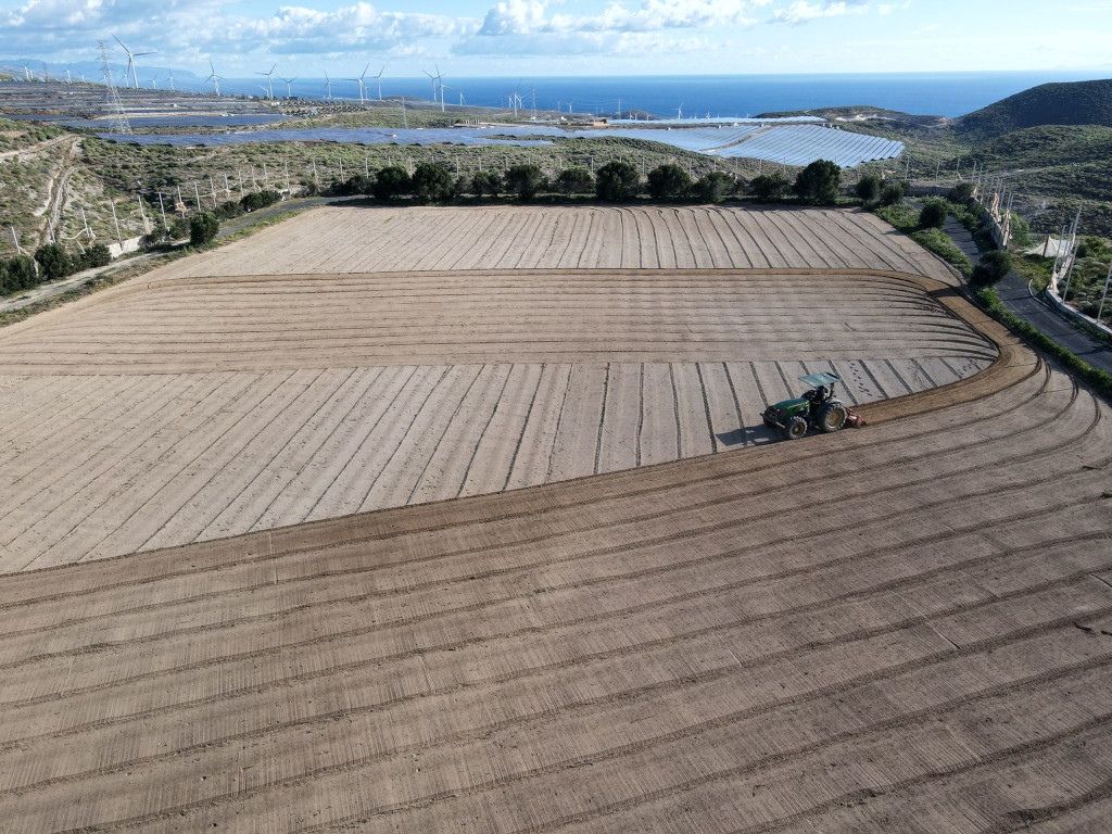 Campo arado con tractor al fondo, molinos de viento y mar en Tenerife.