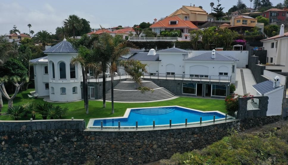 Villa moderna con piscina y jardín en Tenerife, rodeada de casas y palmeras.