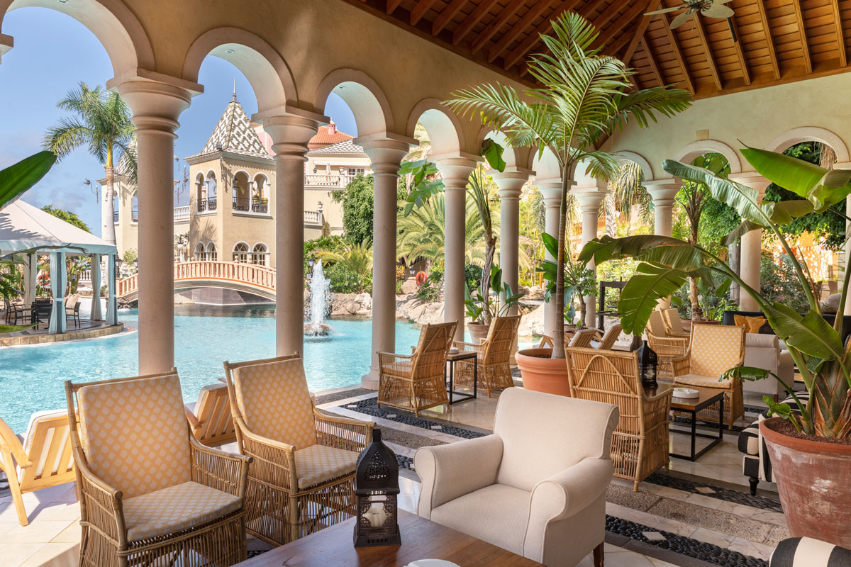 Terraza con piscina y fuente en hotel de Tenerife, rodeada de palmeras.