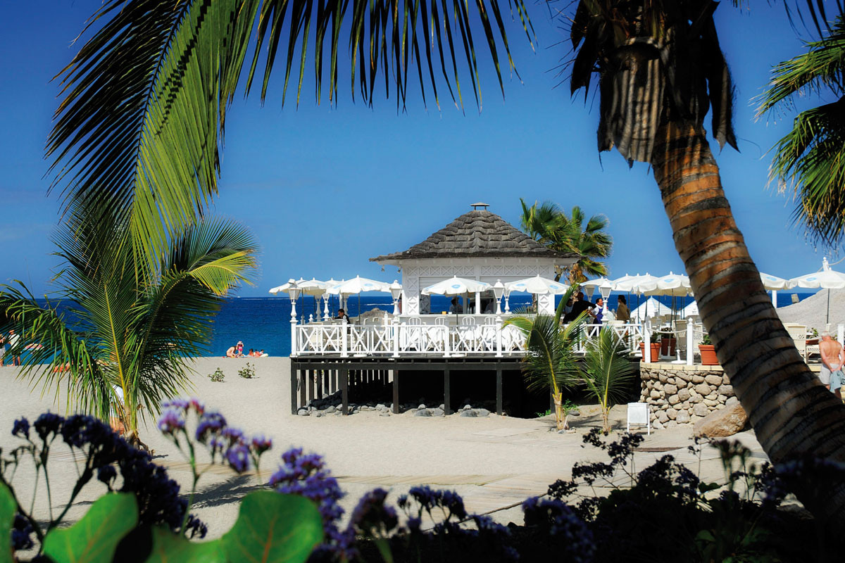 Quiosco blanco en la playa con palmeras y mar azul en Tenerife.
