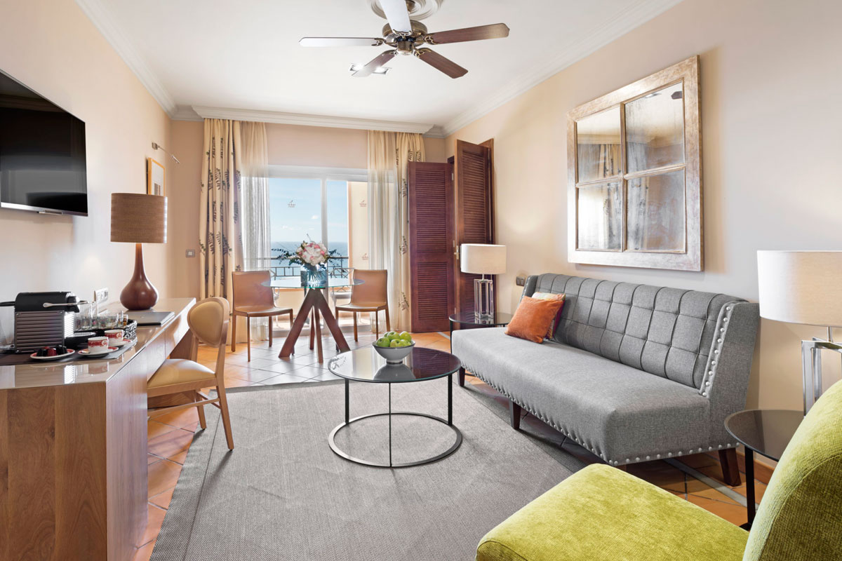 Sala de estar con sofá gris, mesa de vidrio y vista al mar en hotel de Tenerife.
