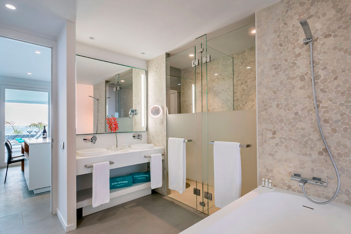 Baño moderno con ducha de vidrio y lavabo doble en un hotel de Tenerife.