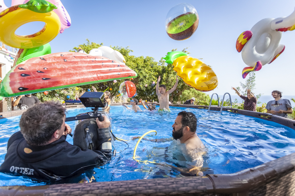 Personas en piscina con flotadores de frutas en Tenerife. Cámara sumergible grabando.