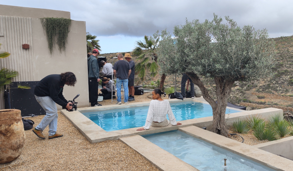 Grupo filmando cerca de piscina en Tenerife. Mujer sentada en el borde.