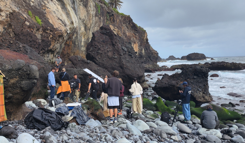 Grupo de personas filmando en una playa rocosa de Tenerife con acantilados al fondo.