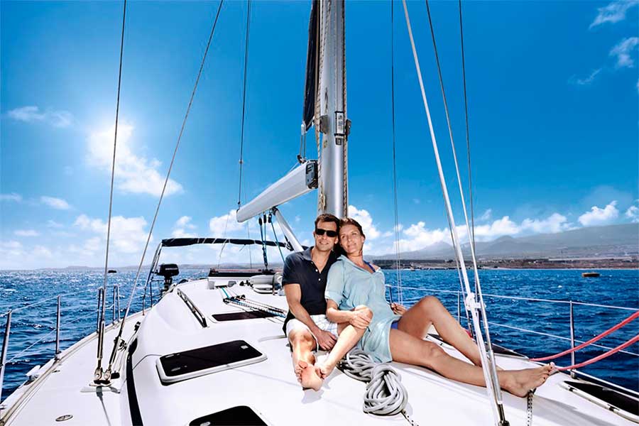 Pareja navegando en velero por la costa de Tenerife bajo un cielo azul.