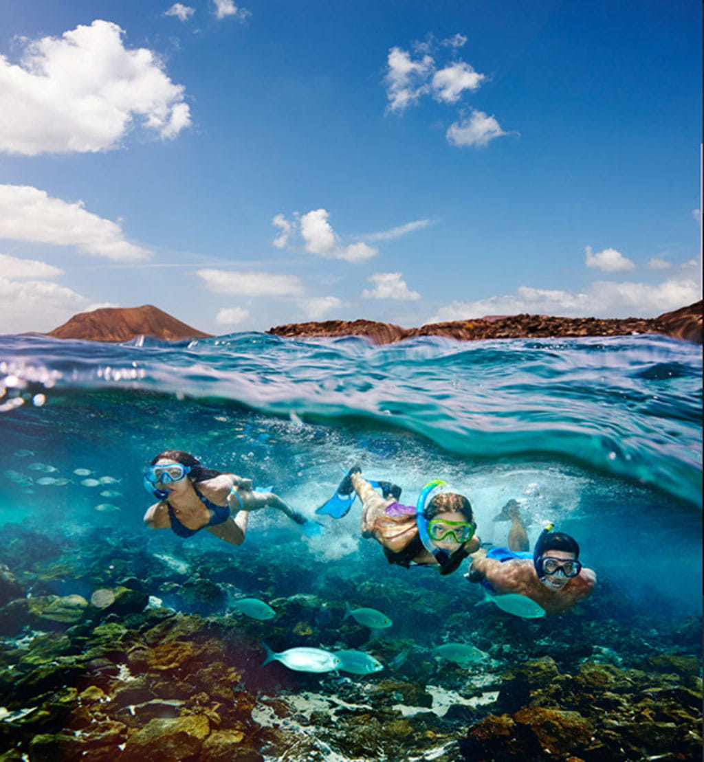 Personas haciendo snorkel en aguas cristalinas de Tenerife bajo un cielo azul.