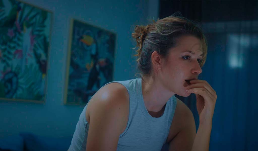 Persona pensativa observando algo en una habitación con cuadros en las paredes.