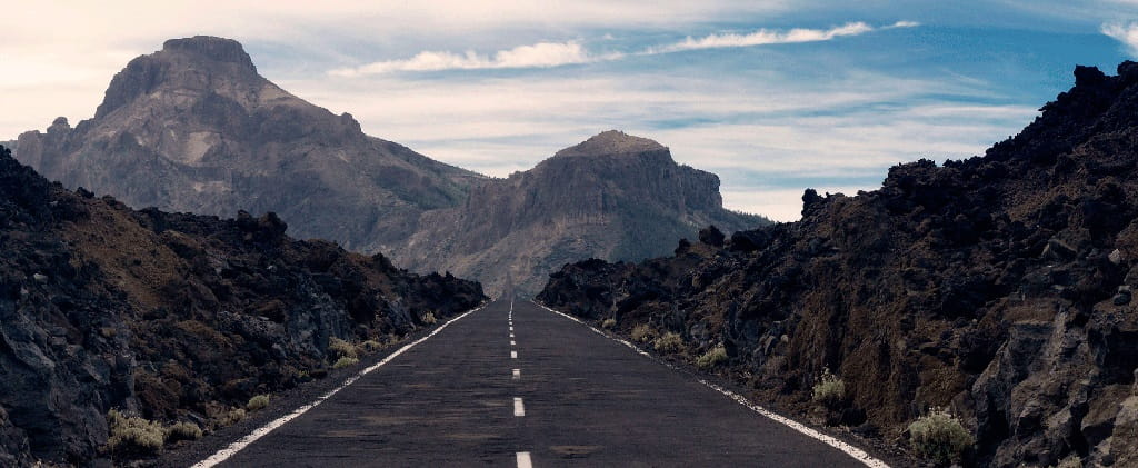 Carretera recta rodeada de paisaje montañoso volcánico en Teide, Tenerife.
