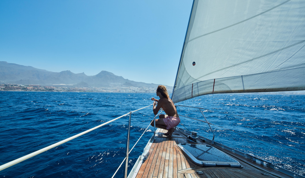 Persona navegando en velero cerca de la costa de Tenerife con montañas al fondo.