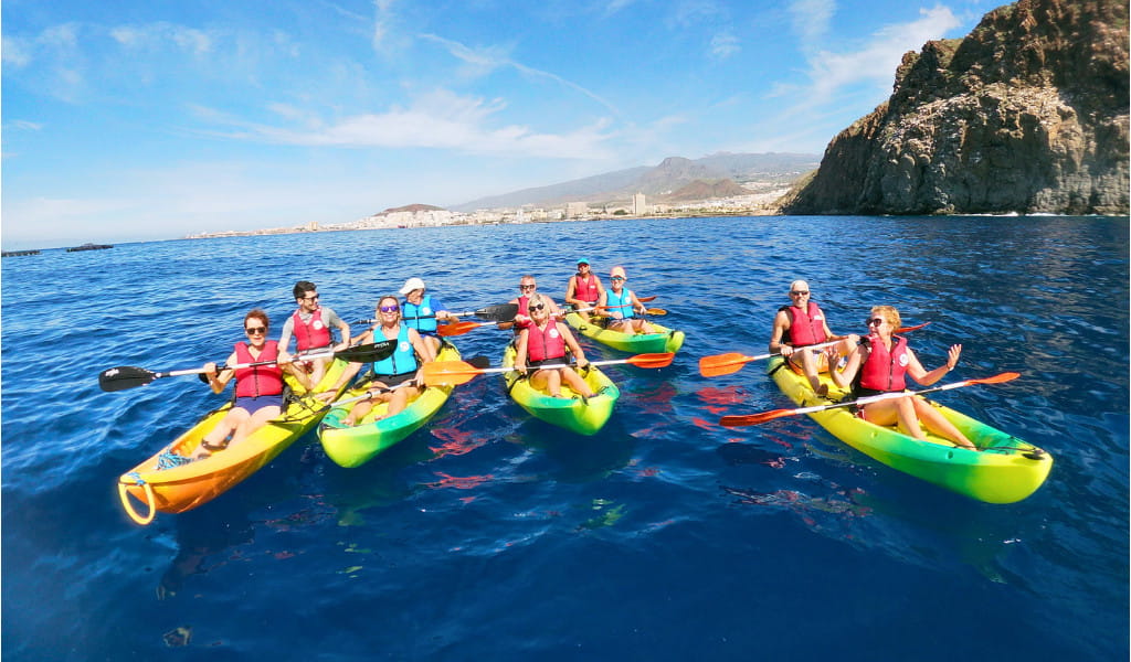 Grupo haciendo kayak en aguas de Tenerife con montañas al fondo.