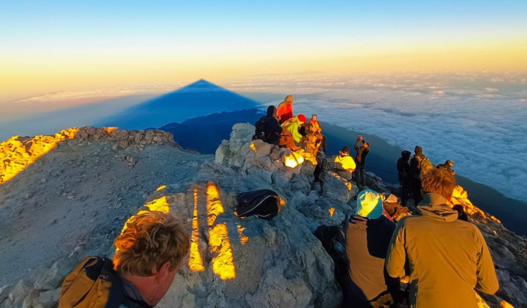 Grupo de personas en la cima del Teide al amanecer, viendo la sombra proyectada sobre las nubes.
