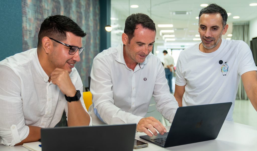 Tres hombres colaboran frente a una computadora en una oficina en Tenerife.
