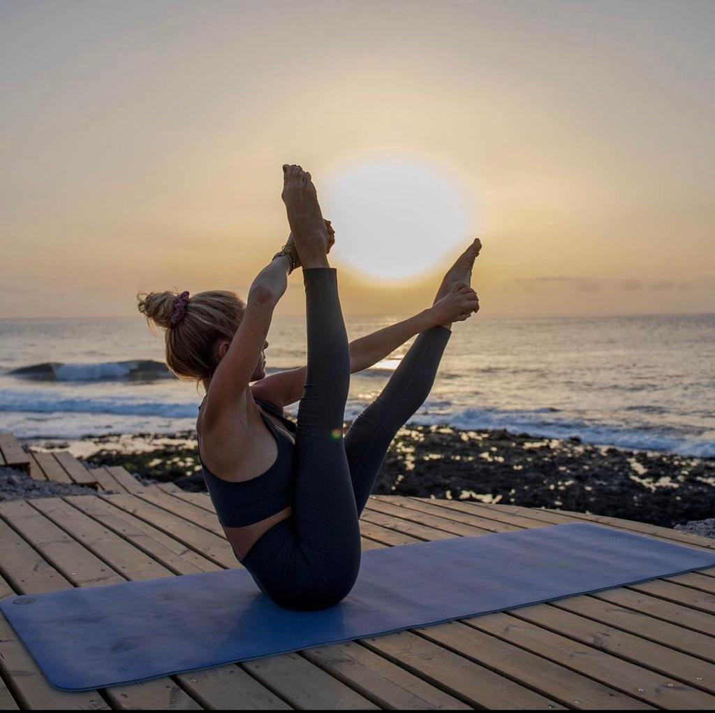 Persona practicando yoga al atardecer en una plataforma junto al mar en Tenerife.