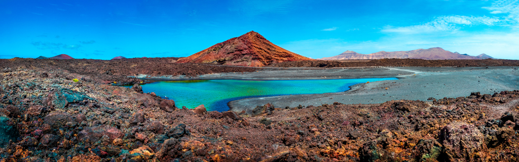 Lago verdoso rodeado de suelo volcánico con montañas al fondo en Tenerife.