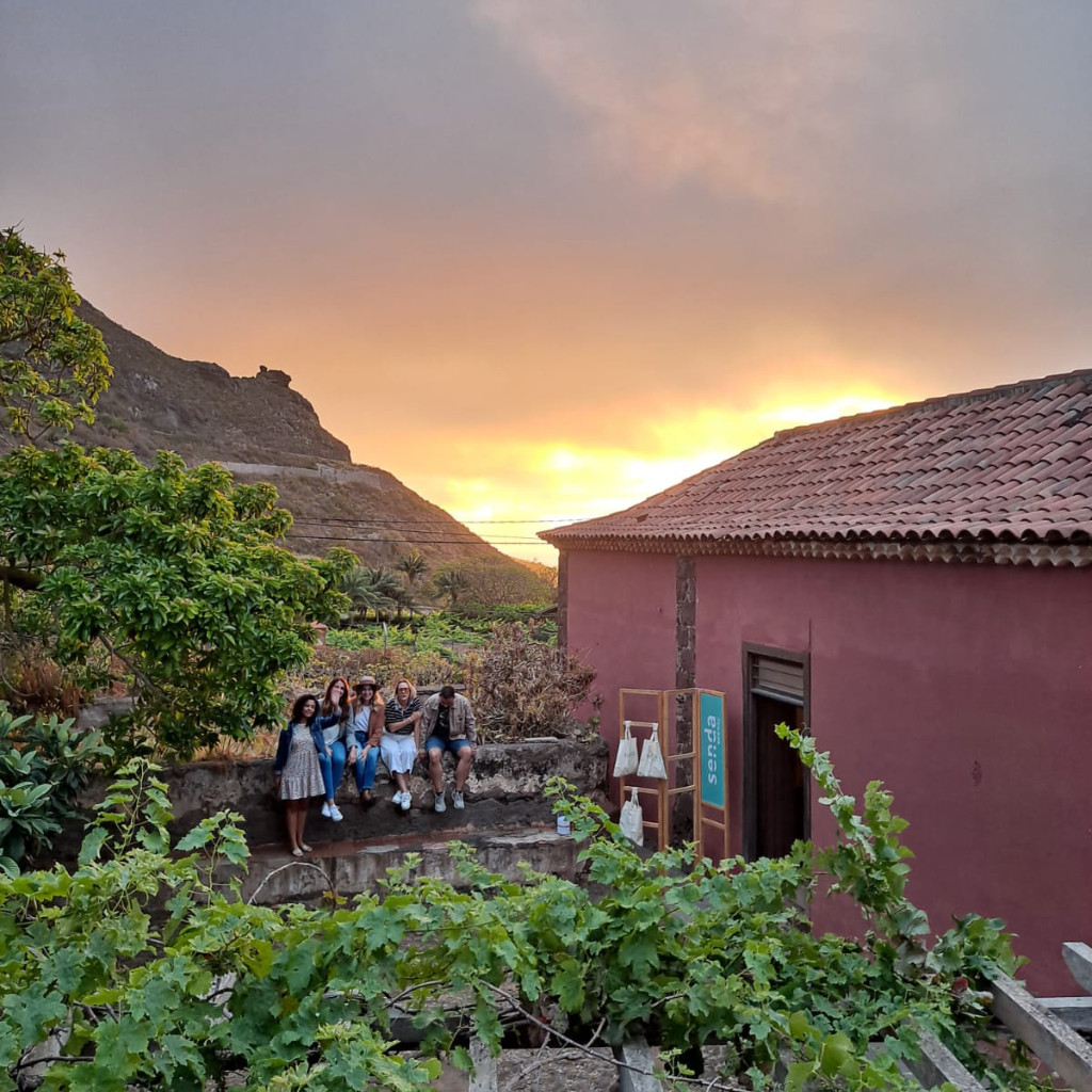 Grupo de personas sentadas al atardecer en un jardín en Tenerife, con cartel senda.