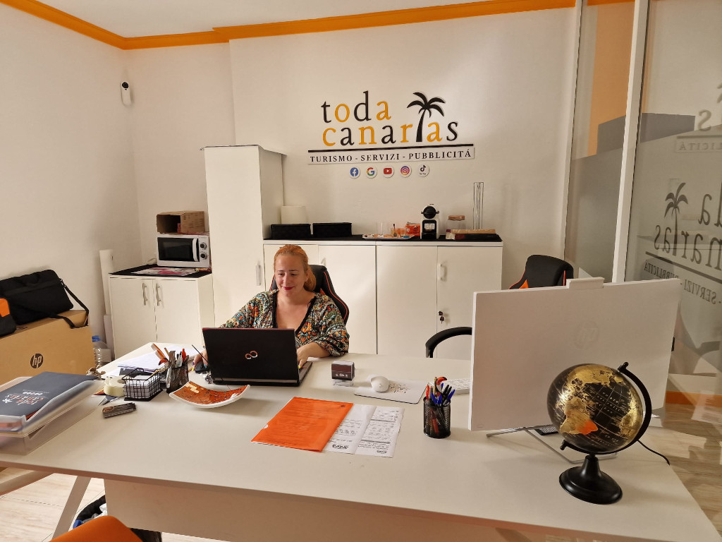 Mujer trabajando en oficina de Toda Canarias, con computadora y papeles en la mesa.