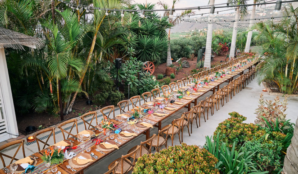 Mesa larga decorada para evento al aire libre en Tenerife, rodeada de palmeras y vegetación.