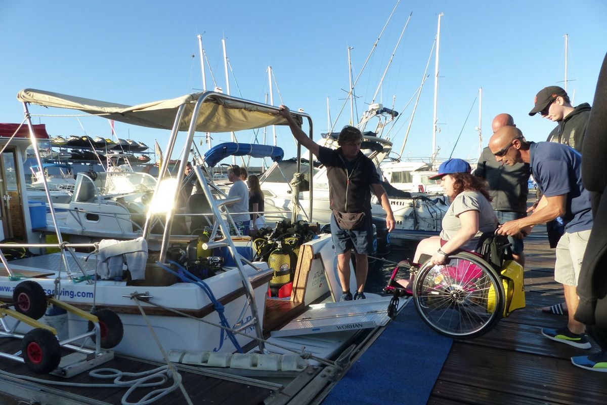 Persona en silla de ruedas abordando un barco en Tenerife con ayuda de varias personas.