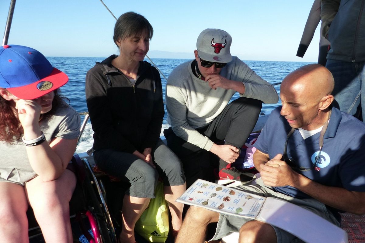 Personas en un barco en Tenerife observan una lista con imágenes y texto mientras navegan.