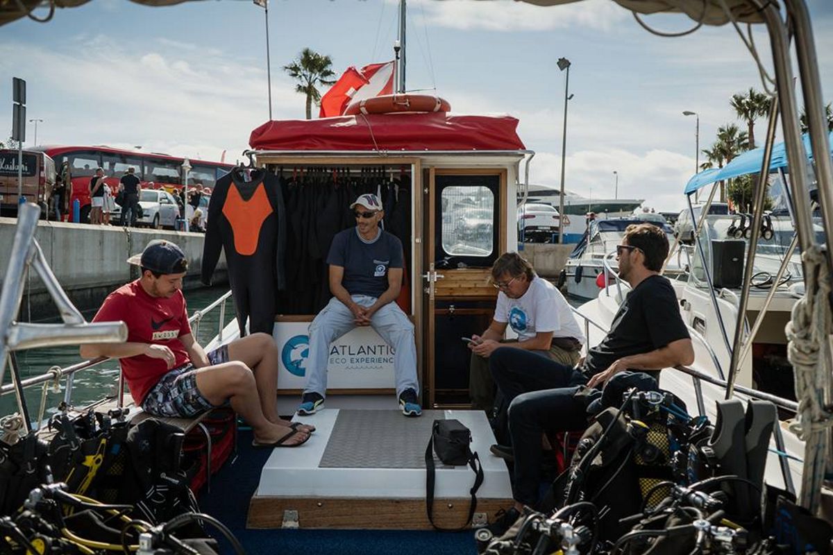 Personas sentadas en un barco de buceo en Puerto Colón, Tenerife, con trajes de neopreno.