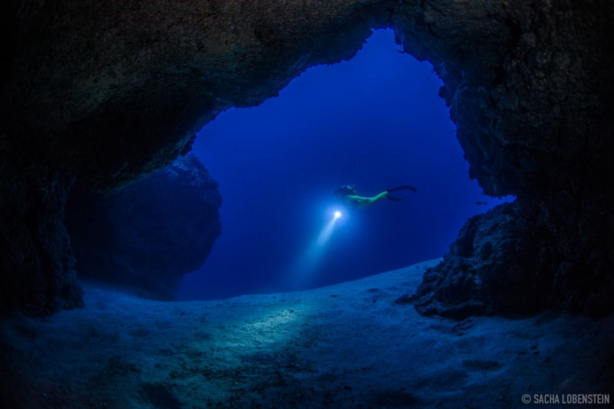 Buceador en cueva submarina iluminando el fondo del océano en Tenerife.