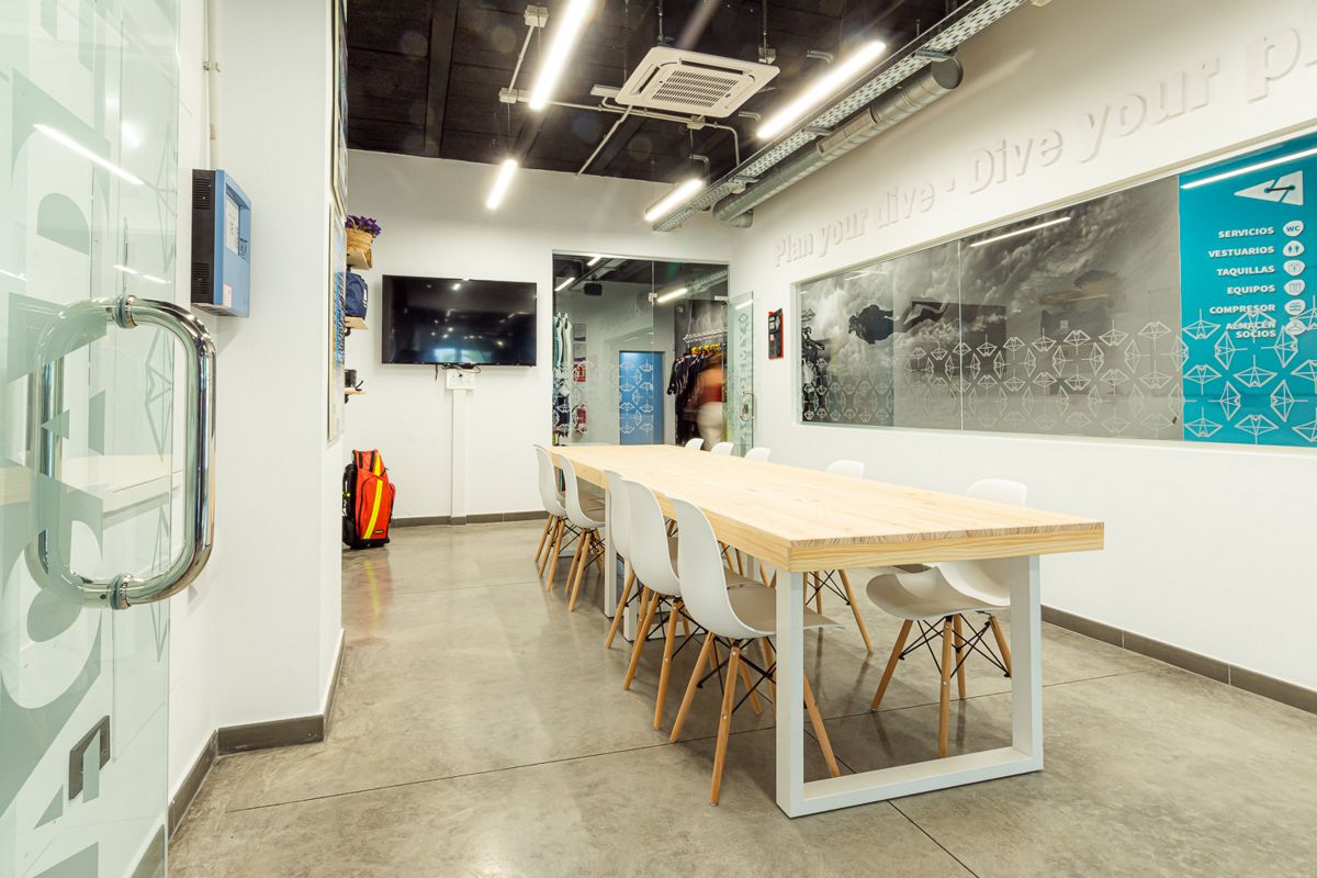 Sala de reuniones con mesa larga y sillas blancas en centro de buceo Tenerife.