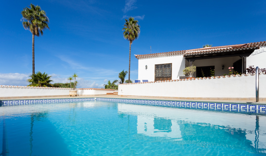 Piscina y casa con palmeras en Tenerife bajo cielo azul.