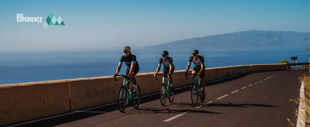 Ciclistas en carretera con océano y vistas de Tenerife. Texto: Bike Experience.